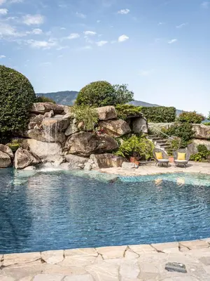 a swimming pool with two chairs and a waterfall at Hotel Olympia in Brunico