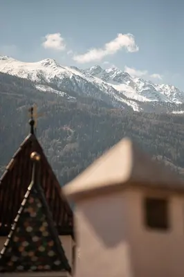 a cross on top of a building with snow covered mountains at Vitalpina Hotel Schulerhof in Plaus