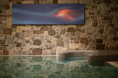 a television hanging on a stone wall with a bench at Vitalpina Hotel Schulerhof in Plaus