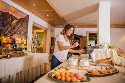 a woman is standing behind a table with food at Wirtshaushotel Alpenrose in San Lorenzo di Sebato