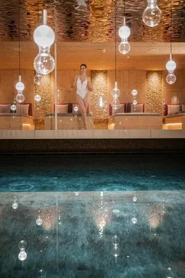 a woman sitting on a couch in front of a swimming pool at Hotel Anewandter in Brunico