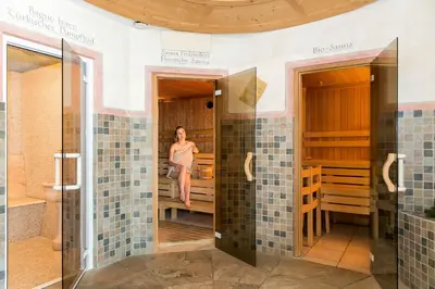 a woman is standing in a bathroom with green tiles at Hotel Cavallino in Badia