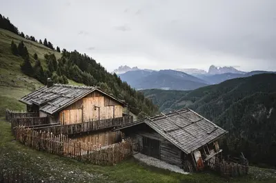 two wooden buildings on a hill with mountains in the background at Hirschhof Pfrein - Hideaway in Chiusa