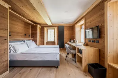 a bedroom with a bed and a desk and a television at Hotel Villa Alpina ***S in Cortina dʼAmpezzo