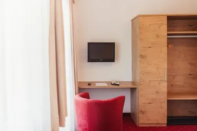 a room with a red chair and a desk with a television at Pension Wiesenrain in Maranza