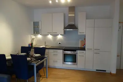 a kitchen with white cabinets and a table with blue chairs at Hager Apartment 2 in Merano