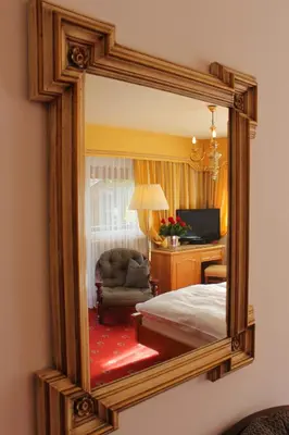 a mirror reflecting a bedroom with a bed and a chair at Villa Martha Vintage Hotel-B&B in Santa Cristina in Val Gardena