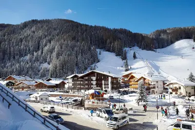 a ski lodge in the snow with cars parked at Hotel Genziana in Selva di Val Gardena