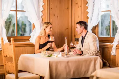 a man and woman sitting at a table with wine glasses at Hotel Genziana in Selva di Val Gardena