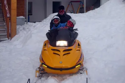 a man and a man riding a snowmobile in the snow at Hotel Valpudra in Selva di Val Gardena