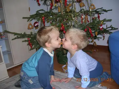 two young boys kissing each other in front of a christmas tree at Hotel Valpudra in Selva di Val Gardena