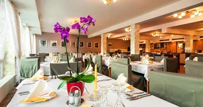 a restaurant with white tables and purple flowers in a vase at Hotel Panoramik in Mühlbach
