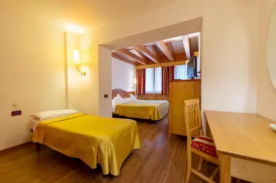 a hotel room with two beds and a table at Hotel Alpino Al Cavalletto in Canazei