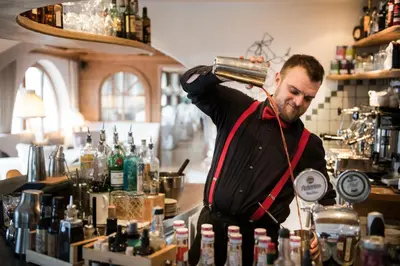 a bartender standing behind a bar with a bottle in his hand at Hotel Mareo Dolomites in San Vigilio Di Marebbe