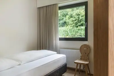 a bedroom with a bed and a window and a chair at Boutique-Hotel Ballguthof am Golfplatz in Lana