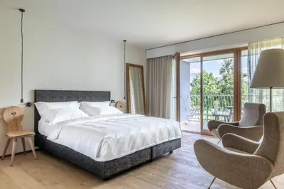 a bedroom with a bed and two chairs and a balcony at Boutique-Hotel Ballguthof am Golfplatz in Lana
