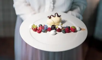 a person holding a plate with fruit on it at Piccolo - Dolomites & Gourmet Hotel in Selva di Val Gardena