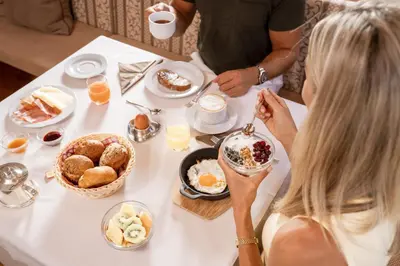 a woman sitting at a table with breakfast foods at Piccolo - Dolomites & Gourmet Hotel in Selva di Val Gardena