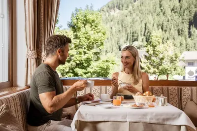 a man and a woman sitting at a table eating food at Piccolo - Dolomites & Gourmet Hotel in Selva di Val Gardena