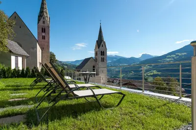 two chairs sitting in the grass next to a church at Panorama Hotel Flora in Villandro