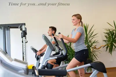 a man and woman riding on an exercise bike in a gym at Hotel Alpenflora in Castelrotto