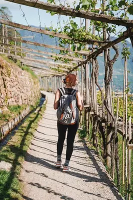 a woman walking down a path with a backpack at Hotel Das Dorner in Lagundo