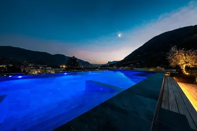 a swimming pool at night with a city in the background at Hotel Das Dorner in Lagundo