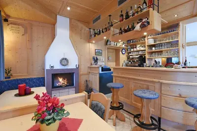 a bar with a fireplace and a table with stools at Alpin-Residence Amadeus in Siusi