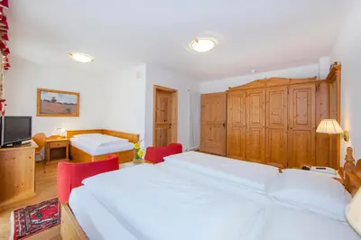 a bedroom with two white beds and a desk at Hotel Corona Krone in Selva di Val Gardena