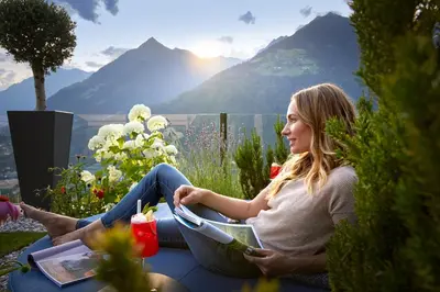 a woman sitting on a balcony with a view of mountains at Hotel Das Sonnenparadies in Schenna