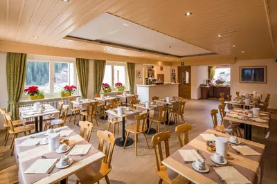 a restaurant with wooden tables and chairs and windows at Garni Bellavista in Arabba