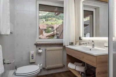 a bathroom with a toilet and a sink and a window at Hotel Ramon in Campitello di Fassa