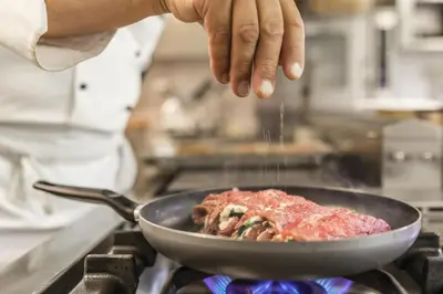 a chef is sprinkling sauce on top of a pan at Pension Prack in Brunico