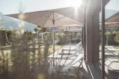 a group of tables and an umbrella on a patio at Hotel Tiefenbrunn Gardensuites & Breakfast in Lana