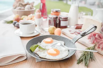two eggs on a plate on a table with a cup of coffee at Hotel Tiefenbrunn Gardensuites & Breakfast in Lana