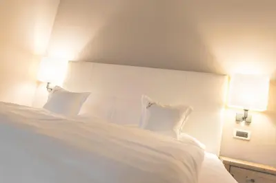 a bedroom with a white bed with two lamps at Hotel Tiefenbrunn Gardensuites & Breakfast in Lana