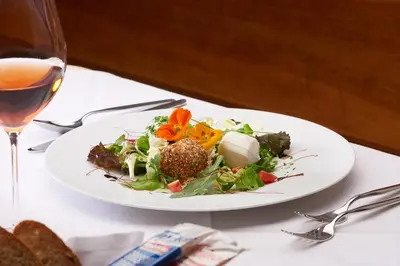 a plate of salad on a table with a glass of wine at Parkhotel Post in Chiusa