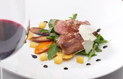 a plate of food with meat and vegetables and a glass of wine at Parkhotel Post in Chiusa