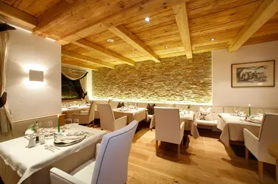a restaurant with white tables and chairs and a stone wall at Savoy Dolomites Luxury & Spa Hotel in Selva di Val Gardena
