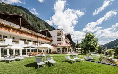 a hotel in the mountains with chairs and umbrellas at Hotel Seeber in Racines