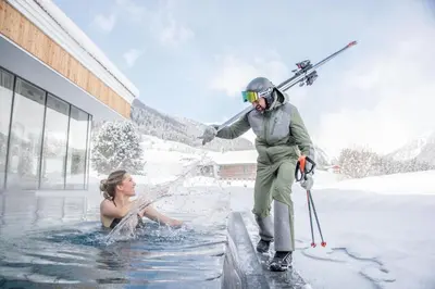 a woman in a pool with a man holding skis at Hotel Plunhof in Ridanna