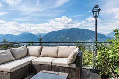 a couch on a balcony with a view of mountains at Hotel Meinhardt in Schenna