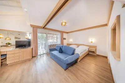 a bedroom with a bed and a blue chair and a television at Residence Villa Gran Baita in Selva di Val Gardena