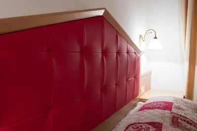 a bed with a red padded headboard in a bedroom at Residence Villa Gran Baita in Selva di Val Gardena