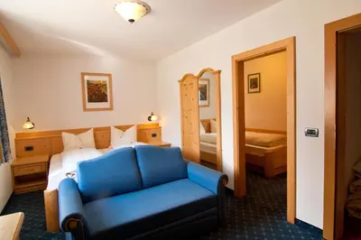 a hotel room with a blue couch and a bed at Pension Enzian in Badia