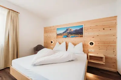 a bedroom with a white bed with a wooden wall at Pension Sonnenhof in Maranza