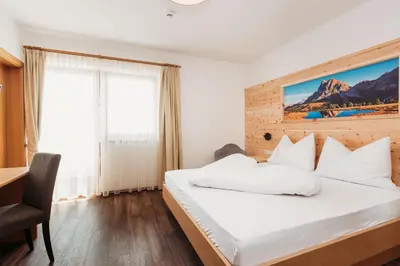 a bedroom with a white bed with a wooden headboard at Pension Sonnenhof in Maranza