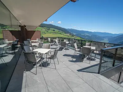a patio with tables and chairs with mountains in the background at Hotel Purvita - Ski In Ski Out - Infinity Pool in Maranza