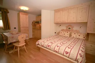 a bedroom with a large bed and a table and a kitchen at Appartamenti Albert in Canazei
