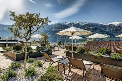 a patio with chairs and umbrellas with mountains in the background at Hotel Belvedere - Adults Only - 14 plus in Naturno